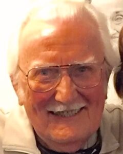 older man with white hair and glasses, smiling.
