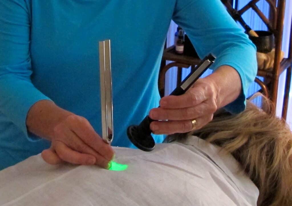 Person holding a light pen and tuning fork to a person's back.